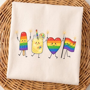 Puede incluir: Una bolsa de mano color crema con personajes de paleta de arcoíris, limonada, corazón y bandera, cada uno sosteniendo bengalas. Los personajes tienen caras sonrientes. La bolsa está sobre un fondo tejido.
