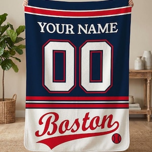 Puede incluir: Una taza de cerámica blanca con un asa negra y el texto "But First, Coffee" en negrita negra. La taza se encuentra sobre un fondo borroso, sugiriendo un ambiente acogedor.