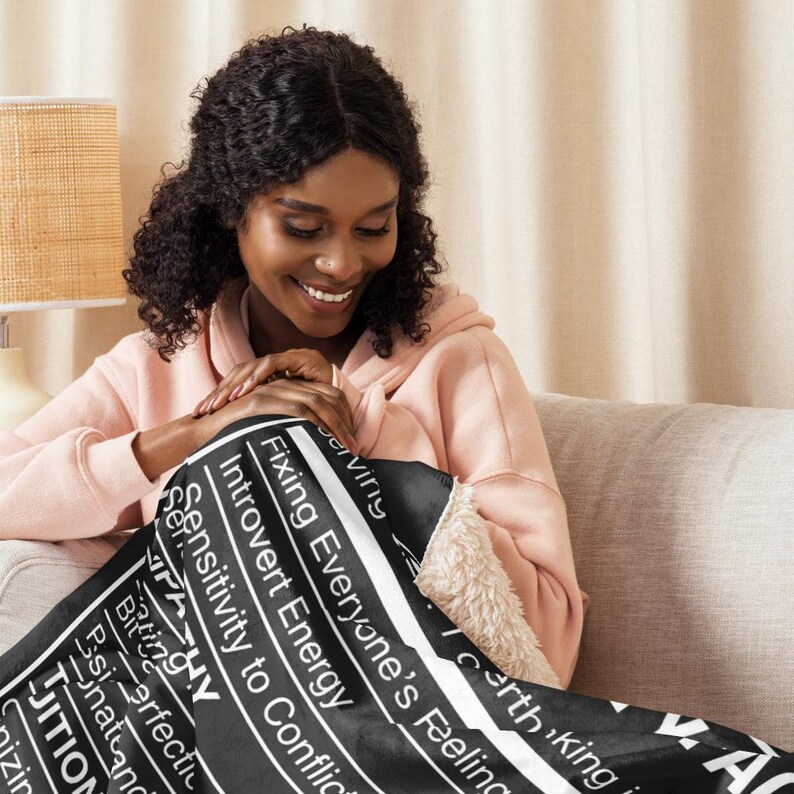 May include: A black and white throw blanket with text, including "Fixing Everyone's Feeling" and "Introvert Energy." The blanket has a soft, fluffy interior and is draped over a person.