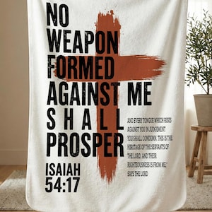 May include: White blanket with the text "NO WEAPON FORMED AGAINST ME SHALL PROSPER" in black, with a rust-colored cross graphic. The text "ISAIAH 54:17" is also included. Additional text is present.