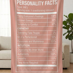May include: A dusty rose blanket with white text that reads "PERSONALITY FACTS" and details about the INFJ personality type. The blanket features a nutrition facts-style design, listing traits like "Introvert Energy" and "Time Alone Required".