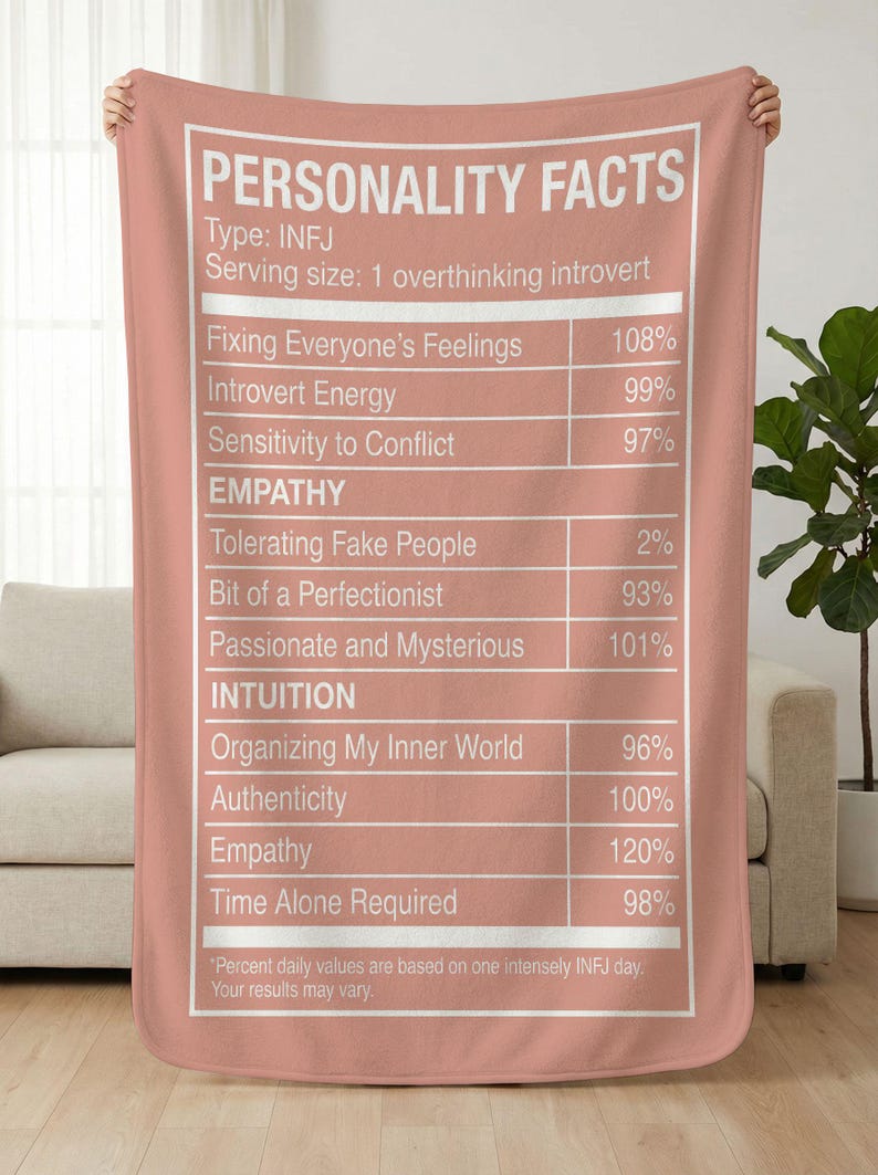 May include: A dusty rose blanket with white text that reads "PERSONALITY FACTS" and details about the INFJ personality type. The blanket features a nutrition facts-style design, listing traits like "Introvert Energy" and "Time Alone Required".