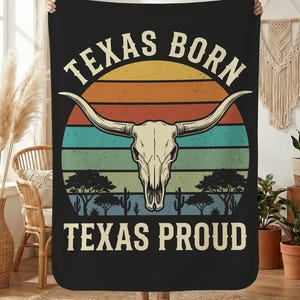 May include: Black blanket featuring a longhorn skull, trees, and cacti set against a sunset design. The text "TEXAS BORN" is above the skull, and "TEXAS PROUD" is below. The blanket is held up by a person.