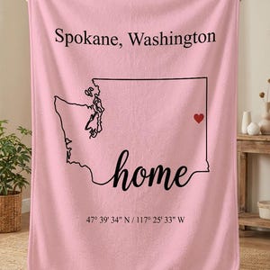 May include: Pink blanket featuring the outline of Washington state with a heart marking Spokane. The word "home" is written in cursive, with the text "Spokane, Washington" above and coordinates below.