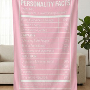 May include: Pink blanket with white text listing "PERSONALITY FACTS" for INFJ personality types. The text includes traits like "Introvert Energy" and "Empathy", with percentage values. The blanket is held up by unseen hands.