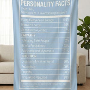 May include: A light blue blanket with white text that reads "PERSONALITY FACTS" and a list of traits with percentages, including "Introvert Energy" and "Empathy". The blanket is held up by a person.