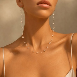Può includere: Delicato set di collana e orecchini in cristallo trasparente. La collana e gli orecchini presentano più cristalli trasparenti di varie dimensioni infilati su fili quasi invisibili, creando un effetto fluttuante. Gioielli indossati.