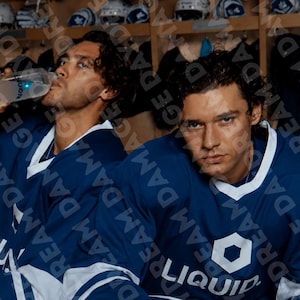 May include: Two individuals wearing blue and white hockey jerseys with the word LIQUID and a hexagon logo printed on the chest. One individual is drinking from a clear plastic water bottle with a blue cap while the other looks forward.