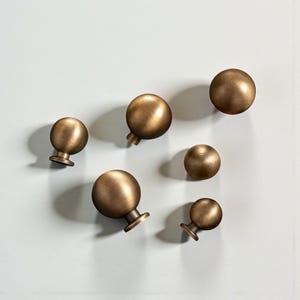 May include: Six bronze-coloured cabinet knobs with a spherical design and textured surface. Each knob has a short, cylindrical base. The knobs are arranged on a light grey background.