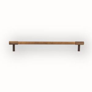 Puede incluir: Un tirador de armario de color bronce con extremos texturizados. El tirador es una barra larga y recta con un centro cil&iacute;ndrico y extremos rectangulares. Los postes de montaje son de color marr&oacute;n oscuro. Aproximadamente 20 cm de largo.