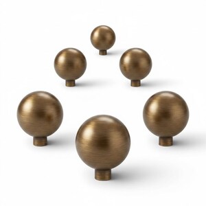 May include: Six bronze-colored cabinet knobs with a spherical design. Each knob has a round base and a smooth, metallic finish. The knobs are arranged against a white background, showcasing their shape and color.
