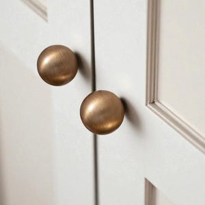 Aged brass drawer knobs installed on white cabinet doors, solid brass knobs for kitchen cabinets