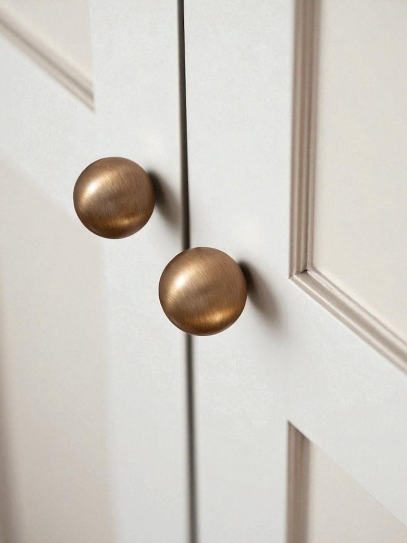 Aged brass drawer knobs installed on white cabinet doors, solid brass knobs for kitchen cabinets