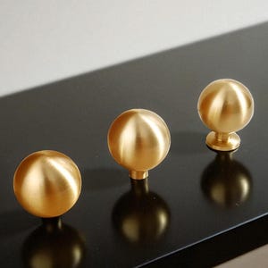 Solid round cabinet knobs on black surface, brushed brass drawer pulls with warm metallic tone