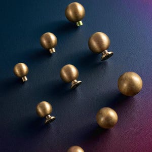 Brushed brass drawer knobs displayed on dark background, solid round cabinet knobs set