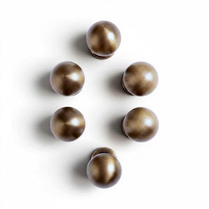 May include: Six antique brass-colored cabinet knobs arranged in a circular pattern against a white background. Each knob is a sphere with a small, round base. The knobs have a warm, metallic finish.