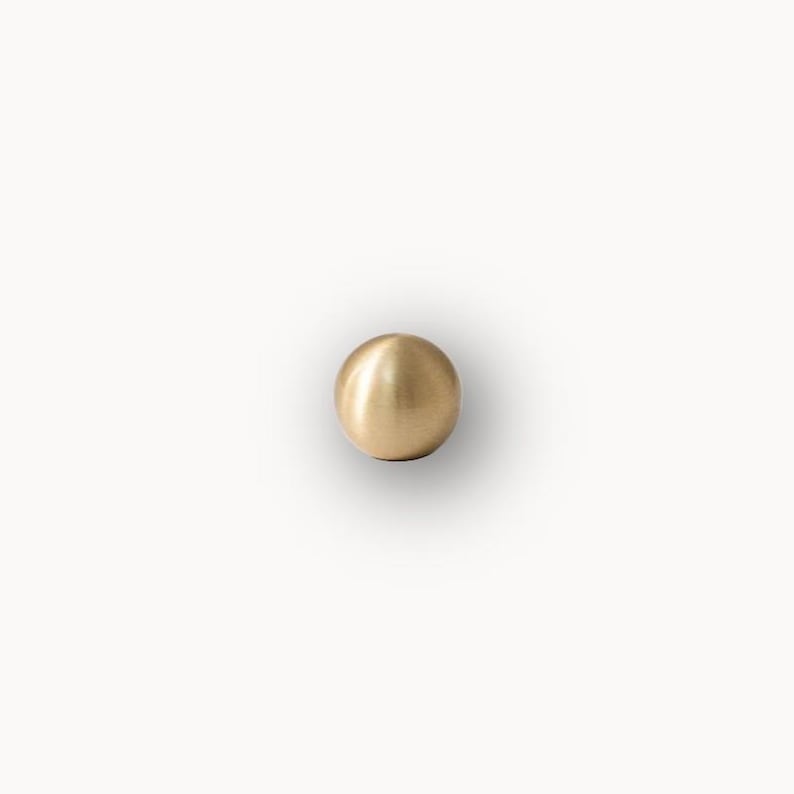 Single solid round cabinet knob, brushed brass drawer pull on light background