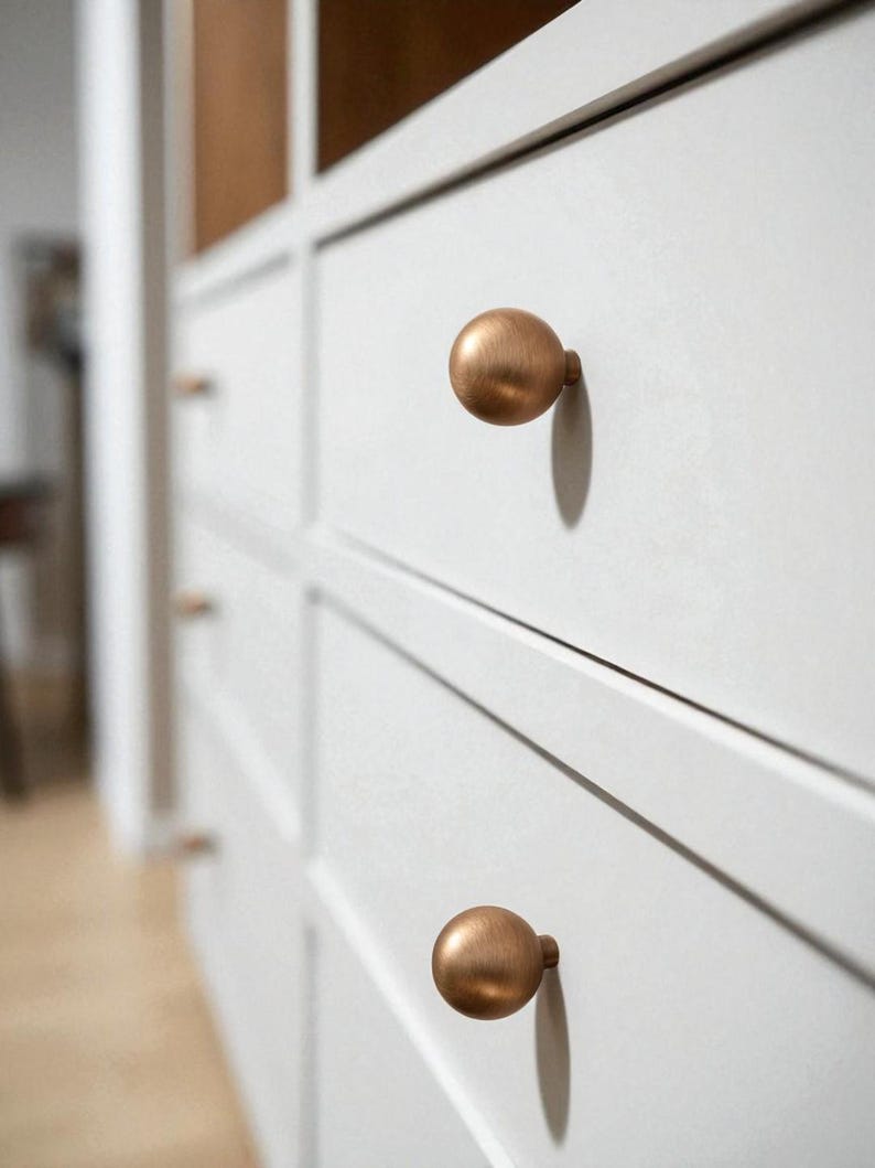 Solid round cabinet knobs installed on white drawers, brushed brass drawer pulls for kitchen and dresser
