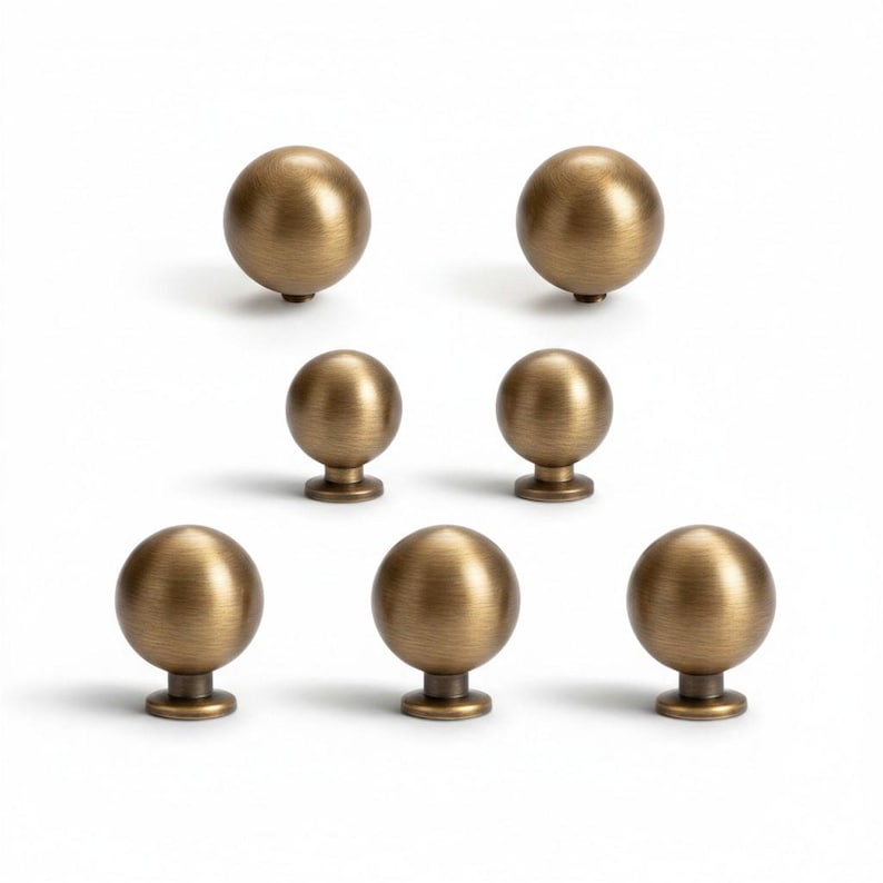 May include: Seven antique brass-colored cabinet knobs arranged on a white background. The knobs are spherical with a short, cylindrical base. The finish has a slightly aged appearance, suggesting a vintage or classic style. Ideal for furniture restoration or adding a touch of elegance.