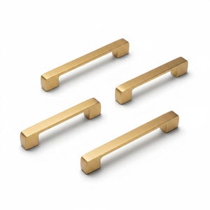 May include: Four gold-colored cabinet pulls arranged on a white background. Each pull is rectangular with rounded edges and a solid, modern design. The pulls are evenly spaced, showcasing their hardware aesthetic.