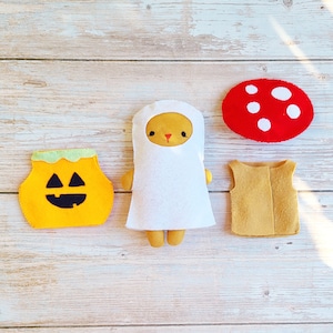May include: A set of felt Halloween costumes for children. The set includes a white ghost costume, a pumpkin costume, a mushroom costume, and a red and white mushroom hat.