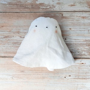 Könnte beinhalten: Ein weißes Geister-Plüschtier mit gestickten Augen und roten Wangen. Der Geist sitzt auf einer hellbraunen Holzoberfläche.