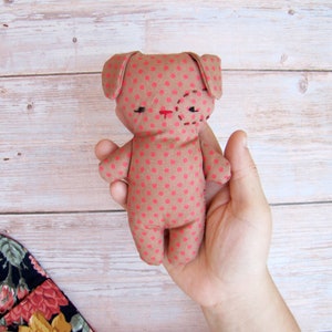 May include: A brown and pink polka dot stuffed animal with a stitched face. The animal has large ears and a small body. It is being held in a person's hand.