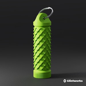 Op de afbeelding: Een limoengroene, cilindervormige sleutelhanger met een textuur van schubben op het lichaam. De bovenkant bevat een metalen ring voor bevestiging en de basis heeft een geribbelde, ronde dop. De tekst Glintworks is zichtbaar in de onderste hoek.