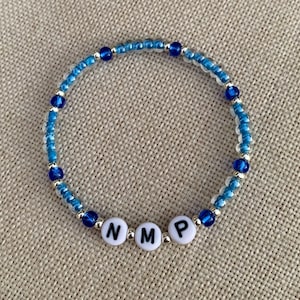 May include: A blue and clear beaded bracelet with the letters "NMP" spelled out in white beads.