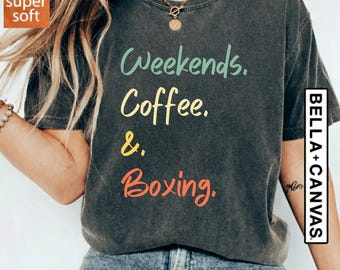 May include: Dark grey t-shirt with the words "Weekends. Coffee. & Boxing." in colourful script. The shirt is from Bella+Canvas and has a "super soft" label. The model is wearing blue jeans.