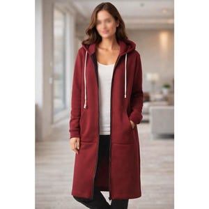 May include: A long, burgundy hooded sweatshirt with a full-length zip and white drawstrings. The sweatshirt has pockets and is worn over a white top and black trousers. The style is casual and comfortable.