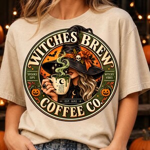 Puede incluir: Una camiseta beige con un gráfico circular de una bruja con sombrero negro sosteniendo una taza humeante. El texto dice Witches Brew Coffee Co. Est. 1692, Spooky Sips, Witchy Vibes y Good Brew Magic Crew. El diseño incluye calabazas y murciélagos.