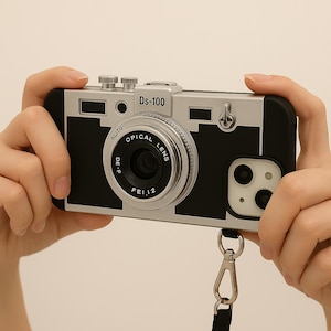 May include: A silver and black phone case designed to resemble a vintage camera. The case features a lens, dials, and the text "Ds-100" and "Alito Optical Lens". A black strap is attached to the bottom.