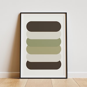 Op de afbeelding: Een ingelijste abstracte kunstprint met een stapel afgeronde rechthoeken in bruin-, beige- en groentinten. Het kunstwerk wordt gepresenteerd in een zwarte lijst tegen een witte achtergrond, met een houten vloer zichtbaar.