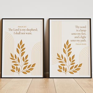 Peut inclure: Deux affiches murales encadrées avec des cadres noirs. Chaque affiche présente un fond crème, des lignes dorées en forme d'arches et une branche feuillue dorée au centre. L'affiche de gauche porte le texte Psalm 23:1, The Lord is my shepherd; I shall not want. Celle de droite porte le texte Psalm 119:105, Thy word is a lamp unto my feet, and a light unto my path.
