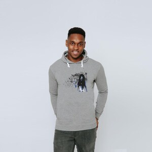 May include: A heather gray long-sleeve hooded sweatshirt featuring a white drawstring and a graphic print on the chest. The graphic depicts a dark, stylized figure surrounded by abstract black ink-like splatters and a small palm tree silhouette.