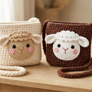 Könnte beinhalten: Zwei handgefertigte Häkel-Umhängetaschen mit Schafgesichtern. Eine Tasche ist cremefarben mit beigem Schafgesicht, die andere dunkelbraun mit weißem Schafgesicht. Beide Taschen haben lange geflochtene Riemen, schwarze Perlenaugen und rosa Wangen.