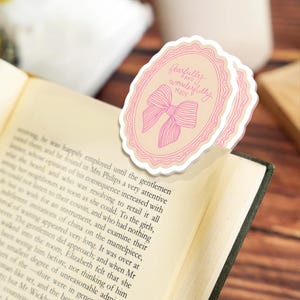 May include: A stack of pink and beige oval-shaped bookmarks with a bow illustration and the text "fearfully and wonderfully made." The bookmarks are placed in an open book with printed text.