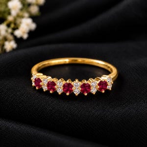 Puede incluir: Un anillo de banda de oro con una fila de rubíes rojos y diamantes blancos redondos alternados. Las piedras preciosas están engastadas en una línea continua en la parte frontal de la banda de oro pulido, creando un contraste entre las piedras.