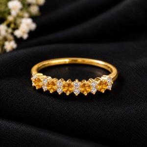 Peut inclure: Une bague en or ornée d'une rangée alternée de pierres précieuses citrines jaunes rondes et de petites pierres blanches transparentes. L'anneau est en or poli et les pierres sont serties en ligne continue sur la moitié avant de la structure.