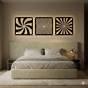 Op de afbeelding: Drie zwarte geometrische wandpanelen met achtergrondverlichting. De ontwerpen omvatten een spiraal, een zonnestraal en een windrad. De panelen zijn gemonteerd boven een bed met een neutraal getint hoofdbord en beddengoed, waardoor een moderne slaapkameresthetiek ontstaat.