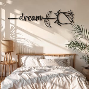 Può includere: Arte da parete in metallo nero con la parola "dream" in corsivo, collegata a una silhouette di rosa. L'opera d'arte è montata sopra un letto con biancheria da letto bianca, creando un arredamento minimalista per la camera da letto.
