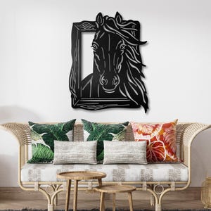 May include: Black metal wall art featuring a horse's head within a rectangular frame. The horse has flowing mane details. The artwork is mounted on a white wall above a wicker sofa with decorative pillows and wooden side tables.