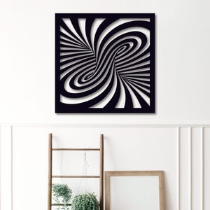 May include: Black and white optical illusion wall art. The artwork features a square frame with a swirling, tunnel-like design. The design is created with alternating black and white stripes, creating a 3D effect. The art is mounted on a white wall.