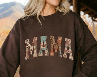 Könnte beinhalten: Ein dunkelbraunes Langarm-Sweatshirt mit Rundhalsausschnitt und dem Wort MAMA in großen Blockbuchstaben auf der Brust. Jeder Buchstabe ist mit einem einzigartigen Muster gefüllt, darunter Leopardenmuster, Kuhflecken und Wüstenmotive.