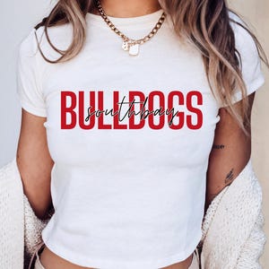 May include: A white crop top with the word "BULLDOGS" in red block letters and "southbay" in a cursive font. The shirt is short-sleeved and has a crew neck.