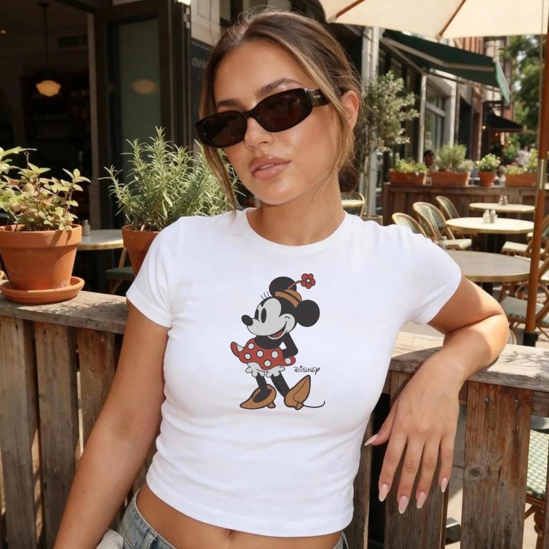 May include: White crop top with a Minnie Mouse graphic. The cartoon character is wearing a red and white polka dot dress, brown shoes, and a flower on her head. The word "Disney" is written below the character.