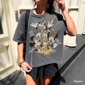 May include: A charcoal gray t-shirt featuring a graphic of Disney characters, including Mickey Mouse, Minnie Mouse, Donald Duck, Daisy Duck, Goofy, and Pluto. The design includes the text "Mickey Mouse" and "Minnie Mouse xoxo".