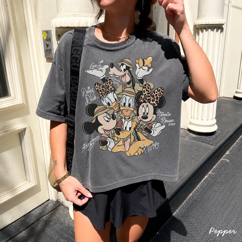 May include: A charcoal gray t-shirt featuring a graphic of Disney characters, including Mickey Mouse, Minnie Mouse, Donald Duck, Daisy Duck, Goofy, and Pluto. The design includes the text "Mickey Mouse" and "Minnie Mouse xoxo".
