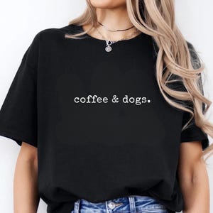 May include: Black t-shirt with the text "coffee & dogs." in a white, simple font. The shirt is a basic crew neck style. The model is wearing blue jeans.